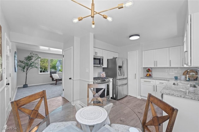 kitchen with appliances with stainless steel finishes, tasteful backsplash, light stone countertops, a sink, and white cabinets