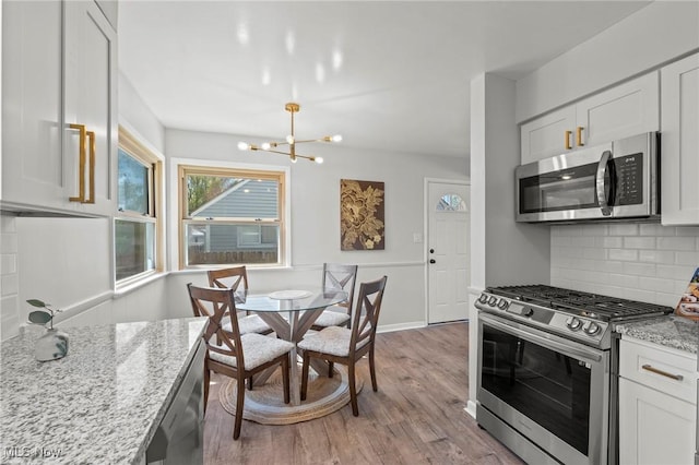 kitchen with appliances with stainless steel finishes, light stone counters, light wood finished floors, a chandelier, and tasteful backsplash