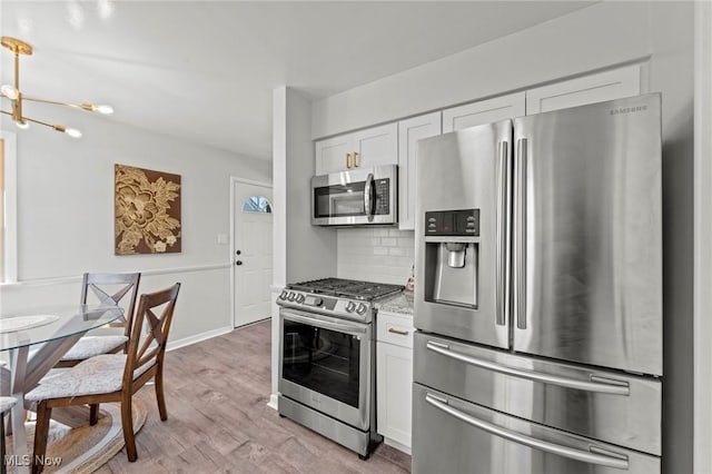kitchen with decorative backsplash, light stone countertops, light wood-type flooring, white cabinets, and stainless steel appliances