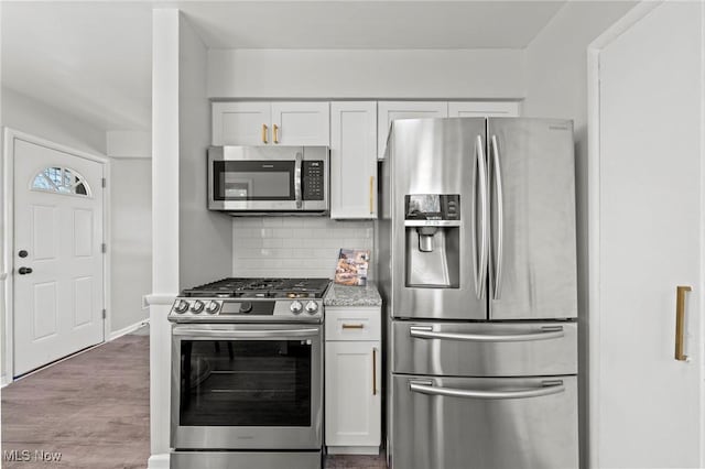 kitchen featuring decorative backsplash, wood finished floors, baseboards, white cabinetry, and stainless steel appliances