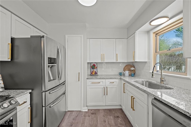 kitchen featuring appliances with stainless steel finishes, tasteful backsplash, white cabinetry, a sink, and light wood-style flooring