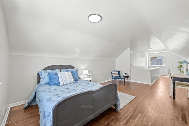 bedroom featuring baseboards, wood finished floors, and lofted ceiling