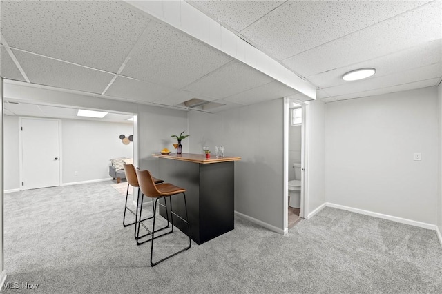bar featuring carpet floors, baseboards, a drop ceiling, and a bar