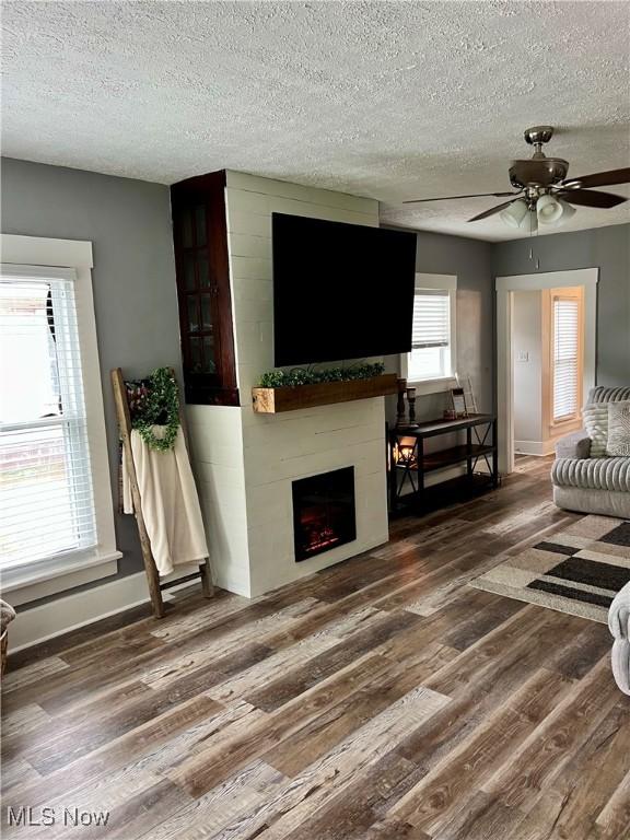living room featuring a textured ceiling, ceiling fan, a fireplace, and wood finished floors