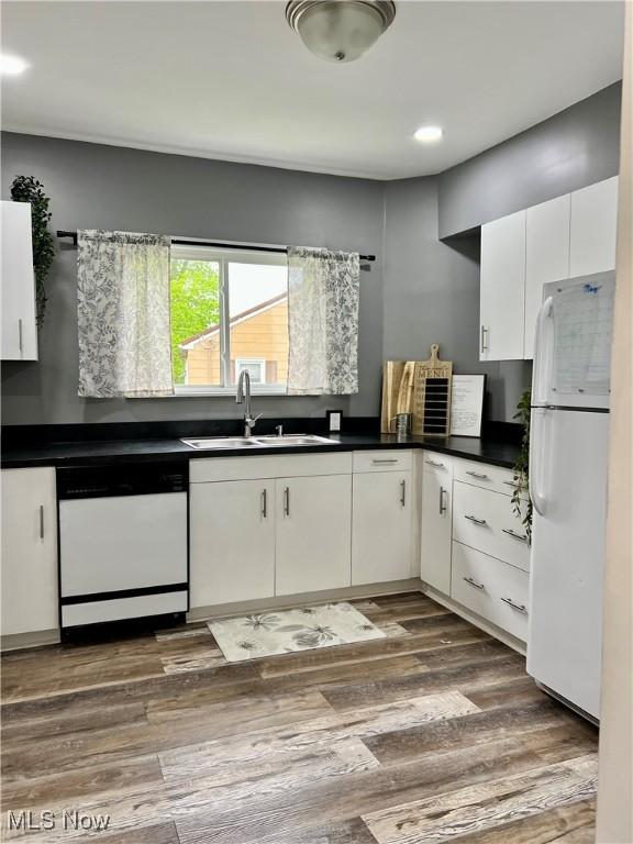 kitchen with dark countertops, a sink, white cabinets, freestanding refrigerator, and dishwashing machine