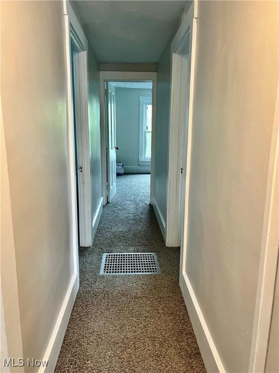 hallway featuring baseboards, visible vents, and carpet
