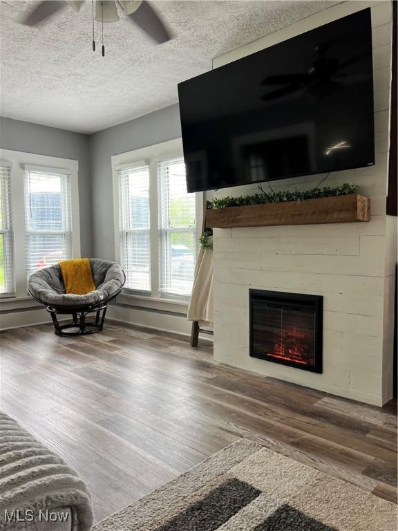 living area with wood finished floors, ceiling fan, a healthy amount of sunlight, and a fireplace