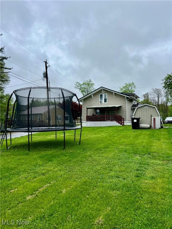 back of house with a lawn, an outdoor structure, a trampoline, and a shed