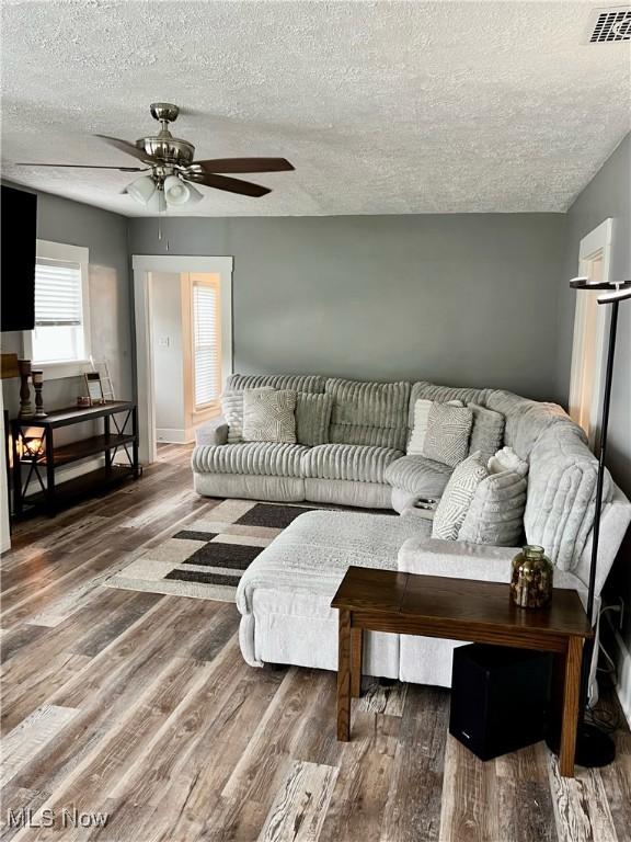 living area with wood finished floors, ceiling fan, a textured ceiling, and visible vents