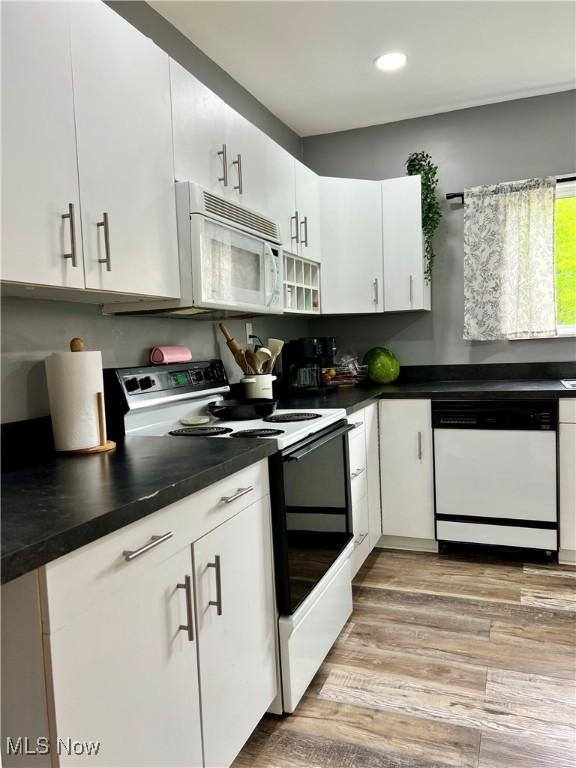 kitchen with white appliances, white cabinetry, dark countertops, and light wood-type flooring