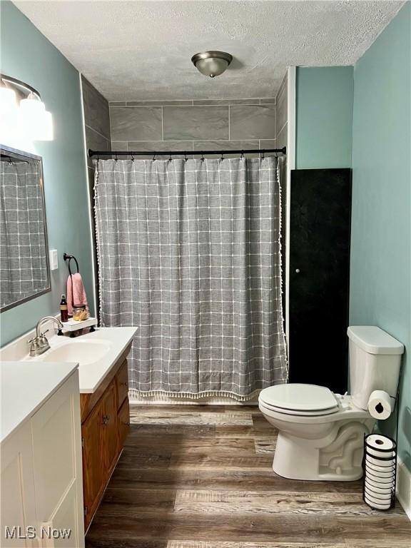 full bathroom featuring a textured ceiling, curtained shower, wood finished floors, vanity, and toilet