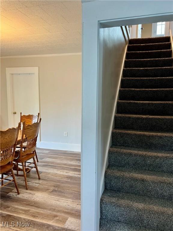 stairs featuring crown molding, baseboards, and wood finished floors