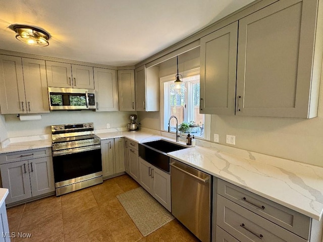 kitchen featuring light tile patterned flooring, appliances with stainless steel finishes, light stone counters, a sink, and gray cabinetry