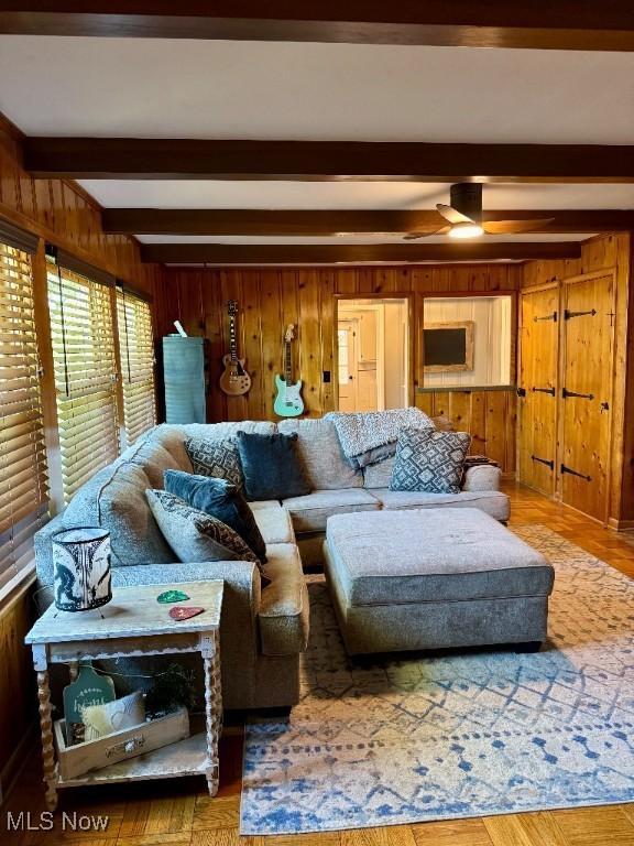 living room with wooden walls, a ceiling fan, beamed ceiling, and wood finished floors