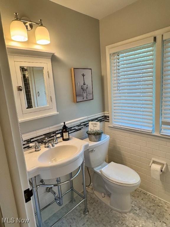 half bathroom featuring a sink, tile walls, wainscoting, and toilet