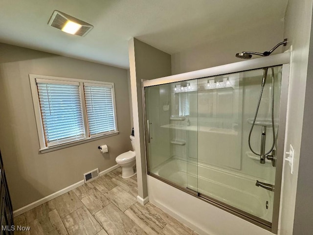 bathroom featuring visible vents, wood finished floors, baseboards, toilet, and shower / bath combination with glass door