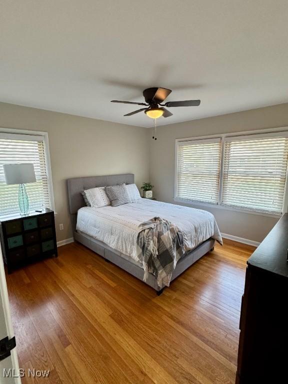 bedroom featuring light wood-style floors, a ceiling fan, baseboards, and multiple windows