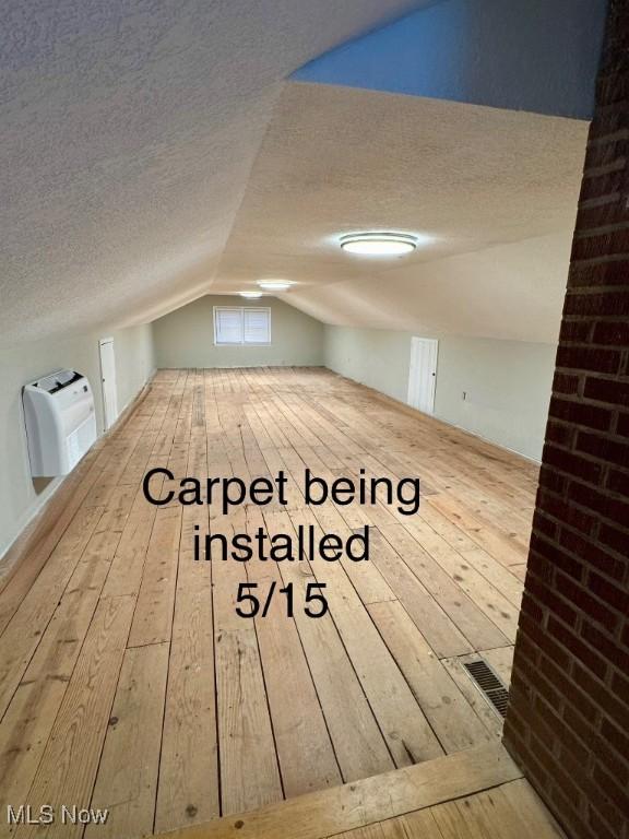 bonus room with a textured ceiling, vaulted ceiling, hardwood / wood-style floors, and visible vents