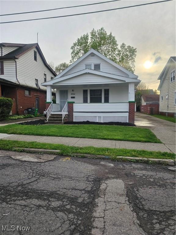 bungalow with a porch, a front lawn, and brick siding