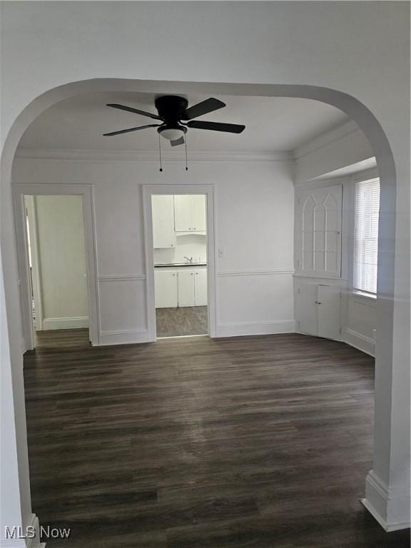 unfurnished room with crown molding, arched walkways, ceiling fan, and dark wood-style floors