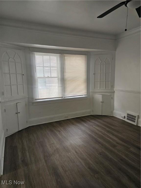 empty room featuring ceiling fan, ornamental molding, dark wood finished floors, and visible vents