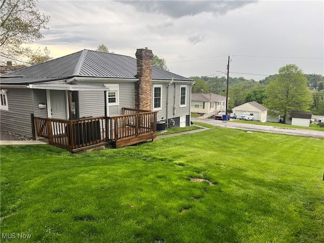 rear view of house with a chimney, metal roof, a lawn, central AC unit, and a wooden deck
