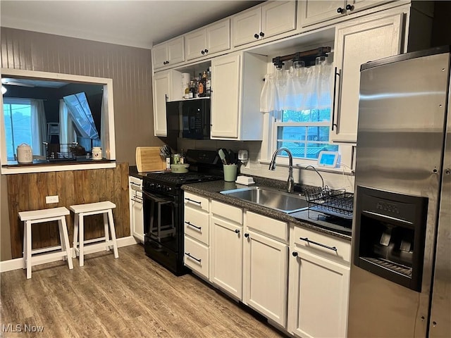 kitchen with wood finished floors, dark countertops, white cabinets, a sink, and black appliances