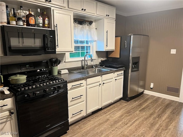 kitchen with white cabinets, dark countertops, a sink, light wood finished floors, and black appliances