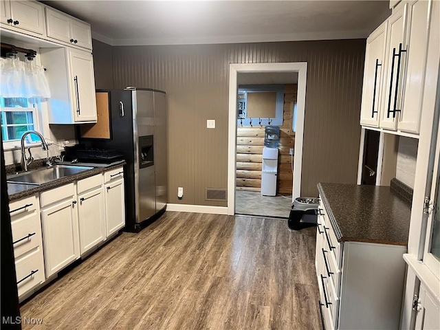 kitchen with dark countertops, stainless steel fridge, a sink, white cabinetry, and wood finished floors