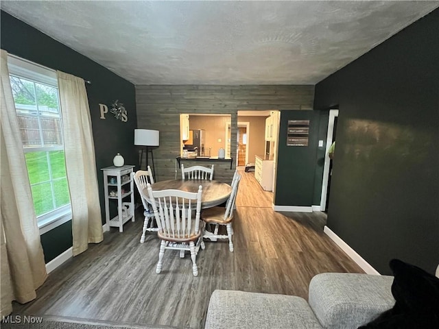 dining area featuring baseboards, wood walls, an accent wall, and wood finished floors