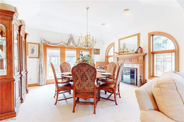 dining space with light colored carpet, a fireplace, vaulted ceiling, baseboards, and a chandelier