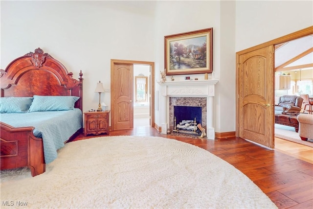 bedroom with wood-type flooring, baseboards, a fireplace with flush hearth, and a towering ceiling