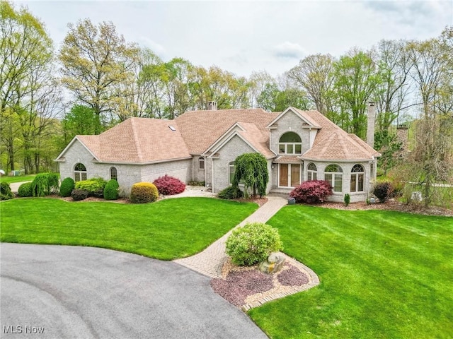 mediterranean / spanish house with brick siding, a front lawn, and a chimney