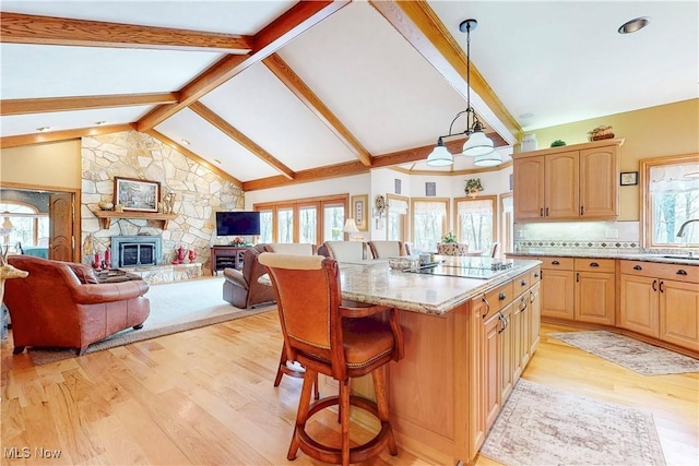 kitchen with a breakfast bar area, a kitchen island, black electric cooktop, light stone counters, and light wood-style flooring
