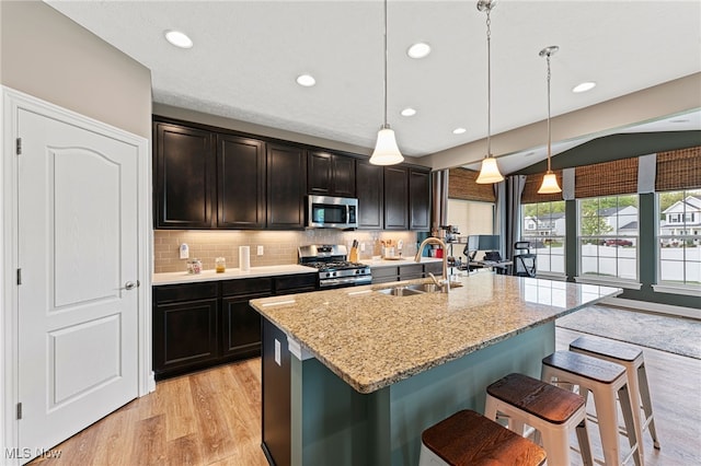 kitchen featuring decorative backsplash, a breakfast bar area, a sink, light wood-style floors, and stainless steel appliances