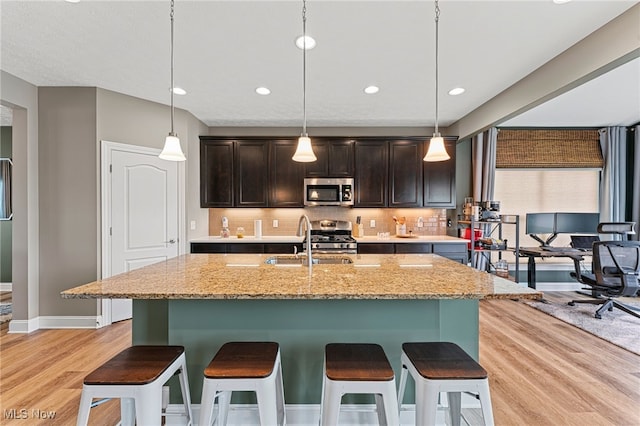 kitchen with dark brown cabinets, a sink, light wood finished floors, a breakfast bar, and stainless steel appliances