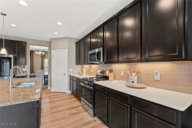 kitchen with hanging light fixtures, a sink, light wood-style flooring, stainless steel appliances, and tasteful backsplash