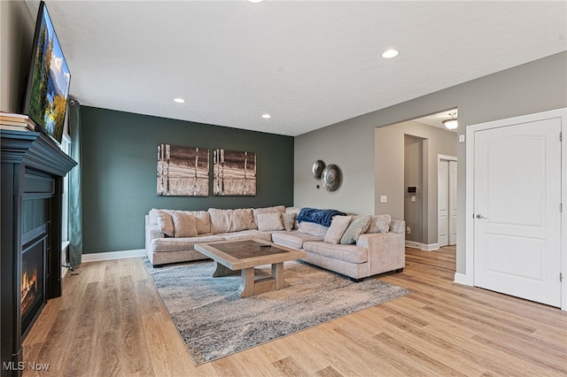 living area featuring recessed lighting, a glass covered fireplace, and wood finished floors