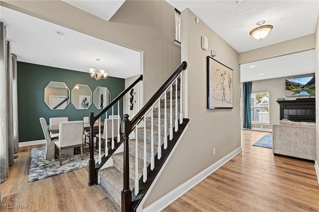 stairway with an inviting chandelier, wood finished floors, a fireplace, baseboards, and a textured ceiling