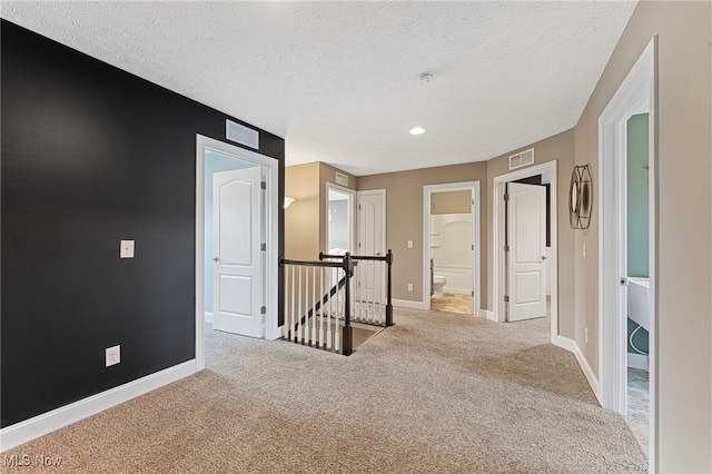 hall with visible vents, carpet, a textured ceiling, and an upstairs landing