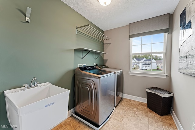 clothes washing area featuring laundry area, baseboards, a textured ceiling, separate washer and dryer, and a sink