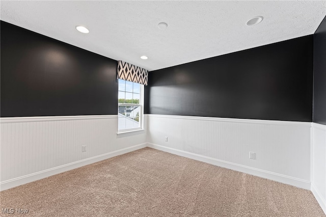 spare room featuring carpet floors, recessed lighting, wainscoting, and a textured ceiling