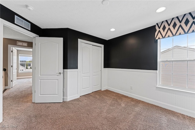 unfurnished bedroom featuring a wainscoted wall, carpet, a closet, and visible vents