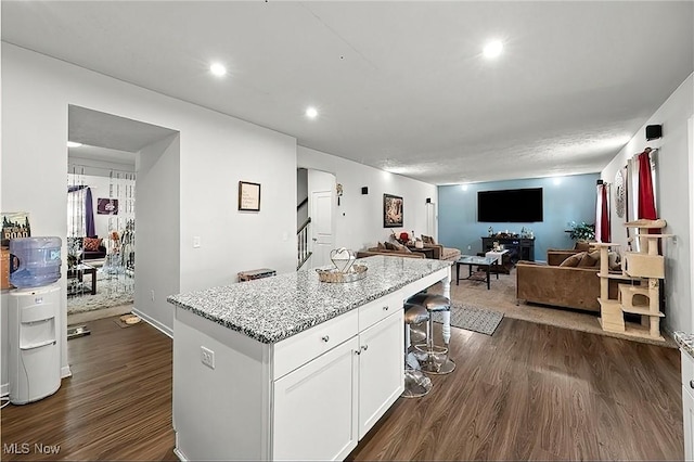 kitchen featuring light stone counters, a center island, white cabinetry, open floor plan, and dark wood-type flooring
