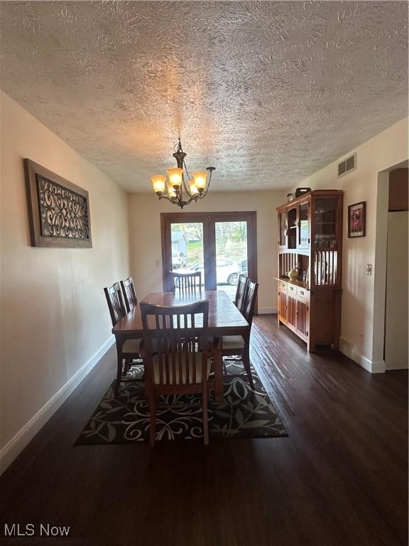 dining room with dark wood-style flooring, a textured ceiling, visible vents, and a chandelier