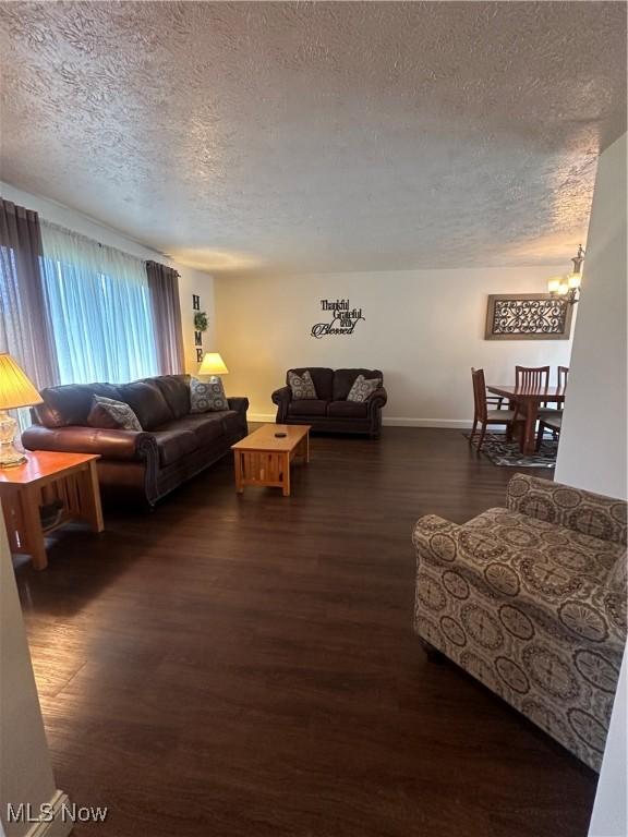 living area with baseboards, dark wood-style flooring, a textured ceiling, and a chandelier