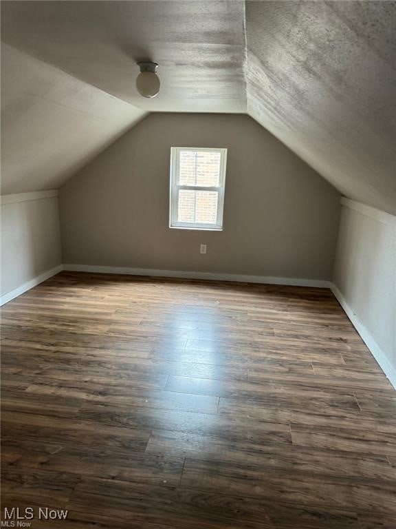 additional living space with baseboards, dark wood-style floors, and lofted ceiling