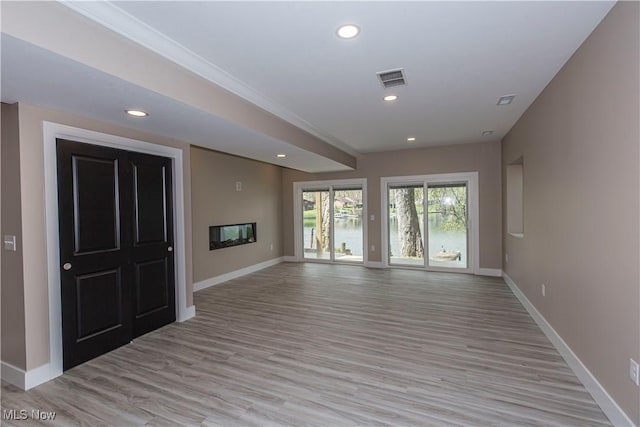 unfurnished living room with crown molding, visible vents, baseboards, recessed lighting, and light wood-style flooring