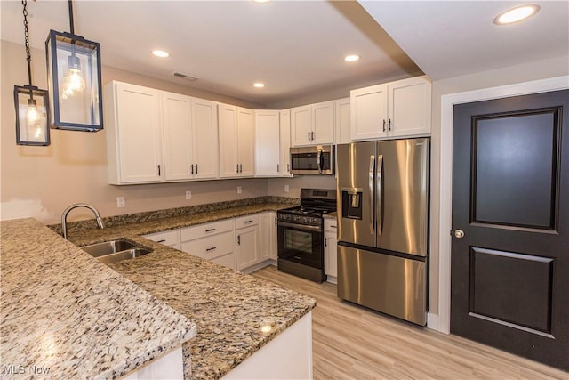 kitchen with visible vents, light stone countertops, white cabinets, a sink, and stainless steel appliances
