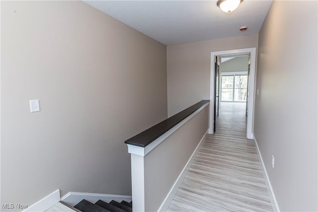 hall featuring baseboards, an upstairs landing, and light wood-type flooring